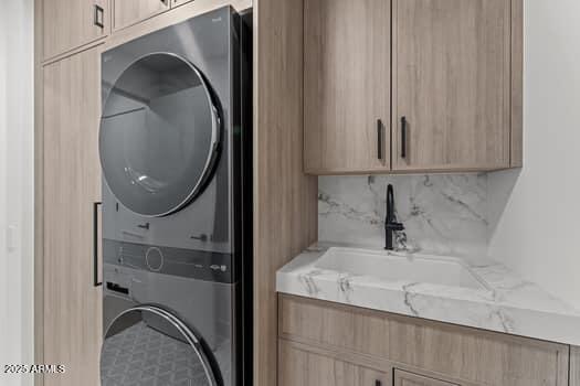 laundry room featuring stacked washer / dryer, cabinet space, and a sink