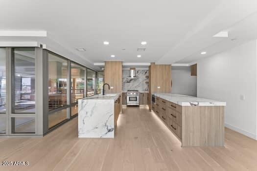 kitchen with modern cabinets, light wood-style flooring, high end stainless steel range oven, a spacious island, and wall chimney range hood