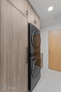 laundry area with stacked washer and dryer, cabinet space, and visible vents