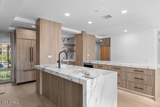 kitchen featuring light stone countertops, a spacious island, paneled built in fridge, recessed lighting, and modern cabinets