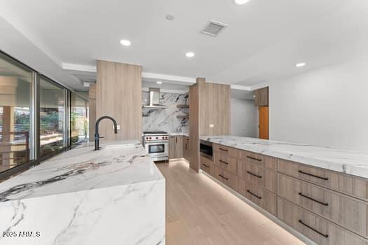 kitchen with high end stove, modern cabinets, wall chimney range hood, and a sink