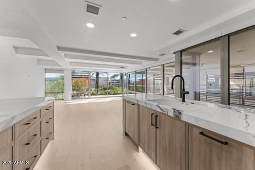 kitchen featuring light stone counters, visible vents, light wood-style flooring, and a sink