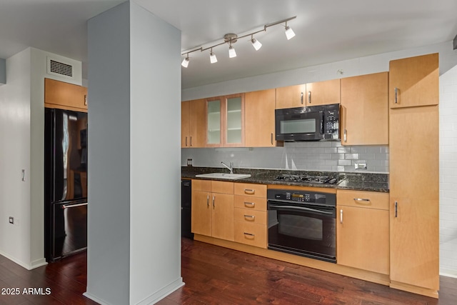 kitchen with light brown cabinets, dark wood-type flooring, dark stone countertops, black appliances, and sink