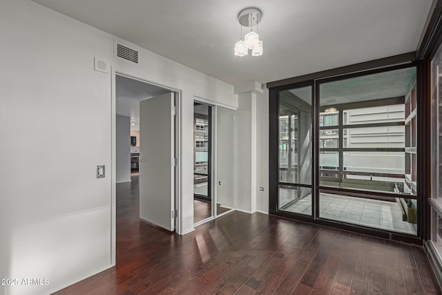 spare room with floor to ceiling windows, dark wood-type flooring, and an inviting chandelier