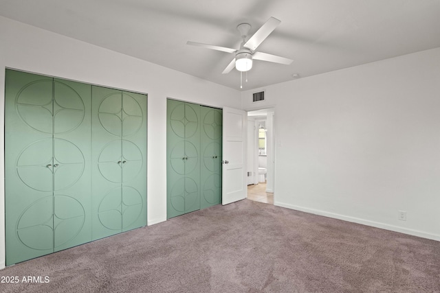 unfurnished bedroom with light carpet, two closets, and ceiling fan