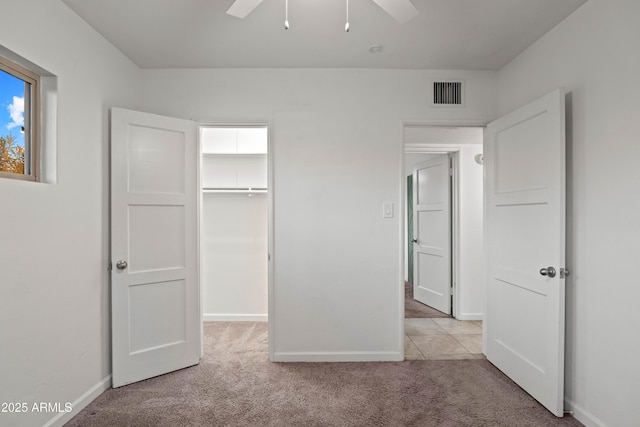 unfurnished bedroom with a walk in closet, light colored carpet, a closet, and ceiling fan