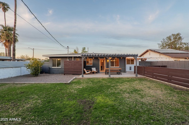 back house at dusk with a yard, a pergola, and a patio area