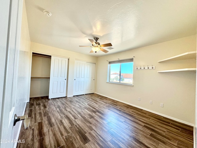 unfurnished bedroom with ceiling fan, dark hardwood / wood-style floors, and two closets