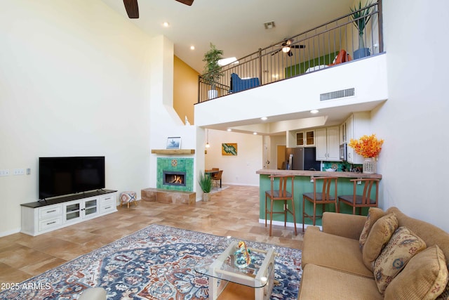 living room featuring ceiling fan, a towering ceiling, and a tiled fireplace