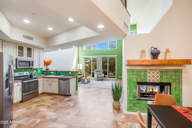 kitchen with kitchen peninsula, white cabinets, stainless steel appliances, sink, and a fireplace