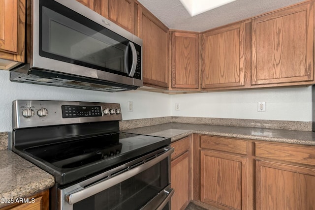 kitchen featuring brown cabinetry, a textured ceiling, and stainless steel appliances