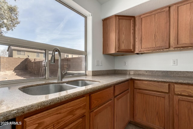 kitchen with a sink, brown cabinets, and light stone countertops