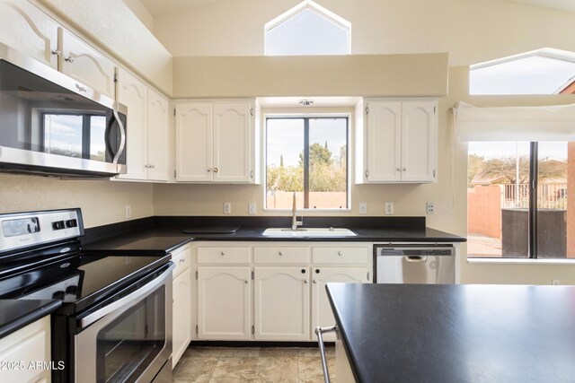 kitchen with dark countertops, white cabinetry, appliances with stainless steel finishes, and a sink