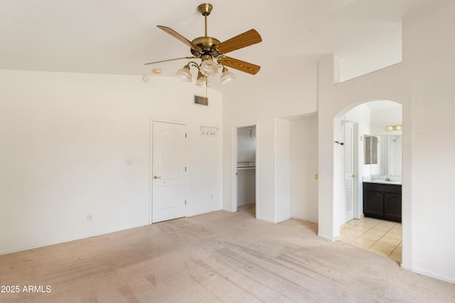 unfurnished bedroom with arched walkways, visible vents, light carpet, a sink, and high vaulted ceiling