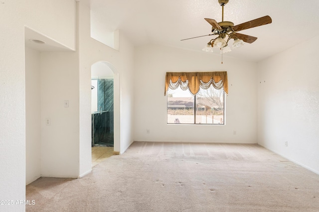 carpeted empty room featuring a ceiling fan, lofted ceiling, and arched walkways