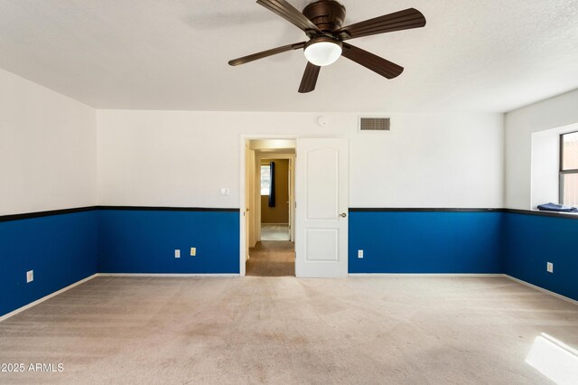 carpeted spare room with visible vents and a ceiling fan