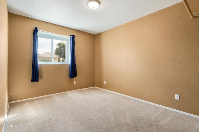 empty room with carpet floors, a textured wall, and baseboards