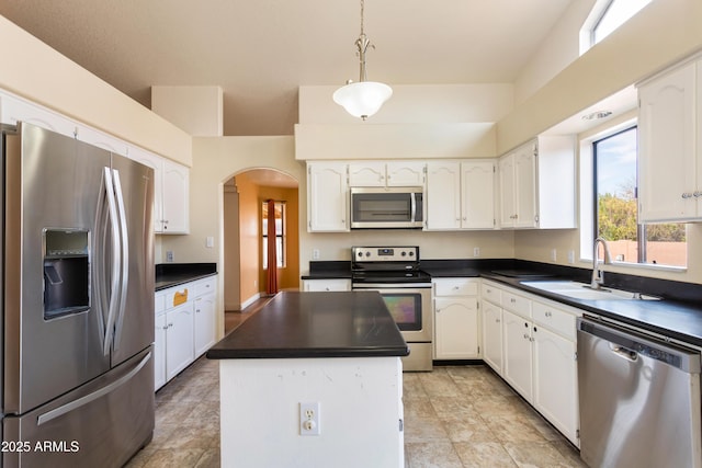 kitchen with arched walkways, stainless steel appliances, a sink, white cabinetry, and dark countertops