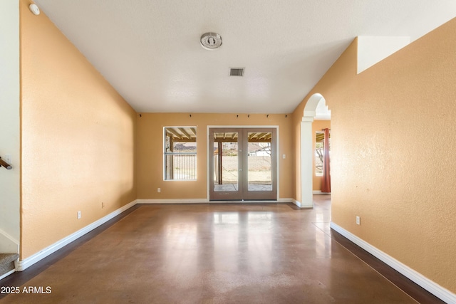 foyer with arched walkways, a textured wall, concrete floors, baseboards, and french doors