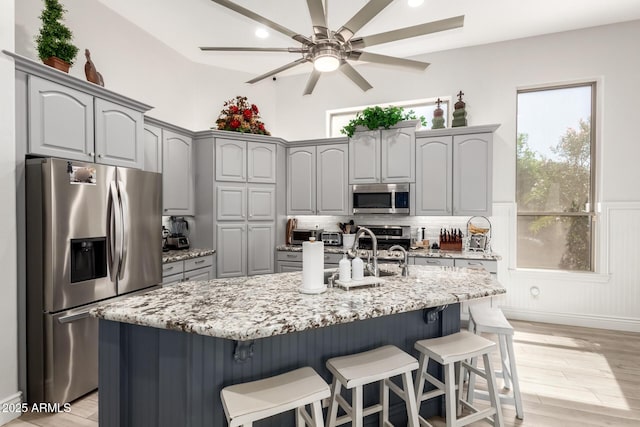 kitchen featuring ceiling fan, light stone countertops, a breakfast bar, gray cabinets, and stainless steel appliances