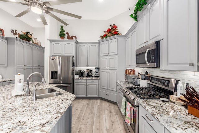 kitchen featuring ceiling fan, appliances with stainless steel finishes, a sink, decorative backsplash, and gray cabinetry