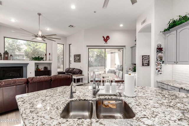 kitchen featuring ceiling fan, light stone counters, a sink, open floor plan, and visible vents