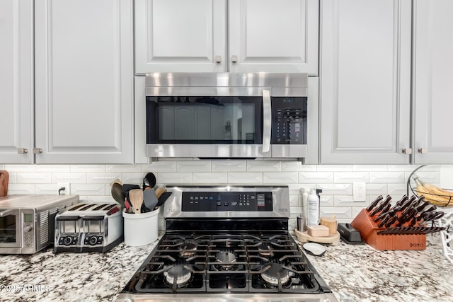 kitchen featuring light stone counters, backsplash, white cabinets, and stainless steel appliances