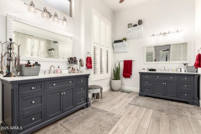 bathroom with a sink, baseboards, two vanities, wood finished floors, and a shower