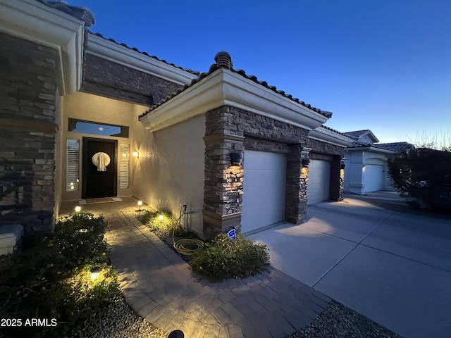 exterior space featuring a garage, stucco siding, driveway, and stone siding