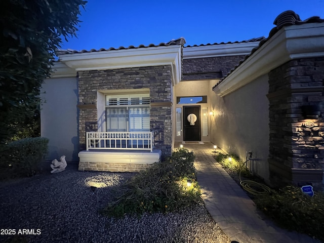 entrance to property featuring a tile roof, stone siding, and stucco siding