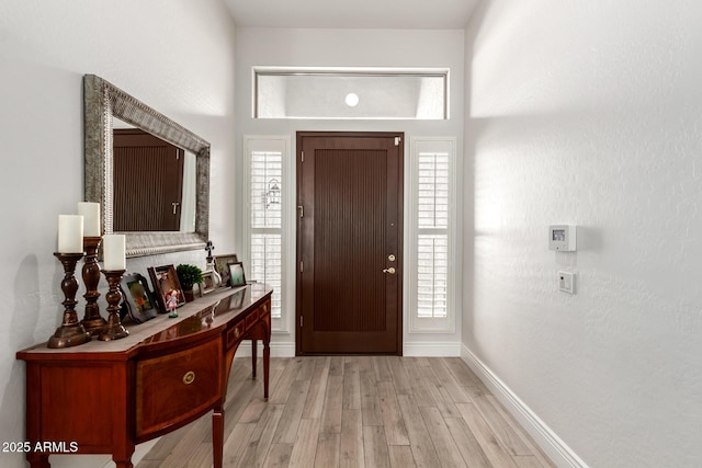foyer featuring baseboards, a healthy amount of sunlight, and light wood finished floors