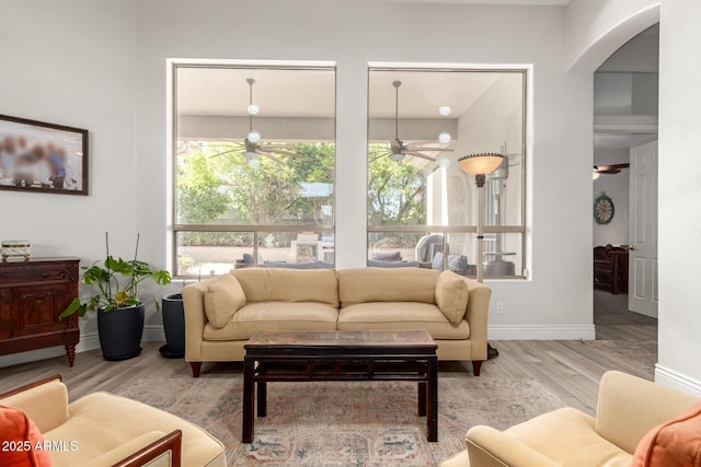 living area featuring a healthy amount of sunlight, arched walkways, a ceiling fan, and wood finished floors