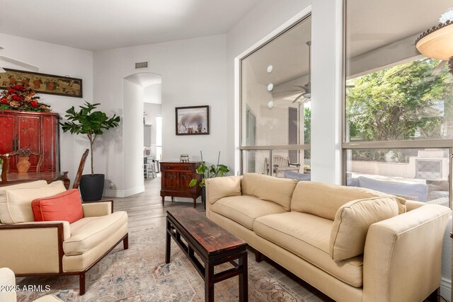 living area with arched walkways, a ceiling fan, wood finished floors, and visible vents