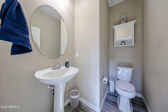 half bath featuring a sink, toilet, baseboards, and wood finished floors