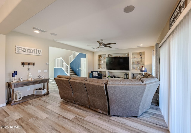 living area featuring built in features, visible vents, ceiling fan, stairs, and light wood-type flooring