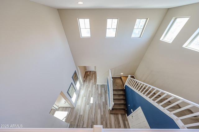 stairs with recessed lighting, a high ceiling, and wood finished floors