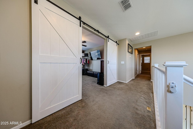 hallway featuring a barn door, baseboards, carpet, and visible vents