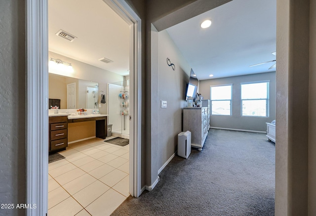 hallway with light tile patterned flooring, light colored carpet, visible vents, and baseboards