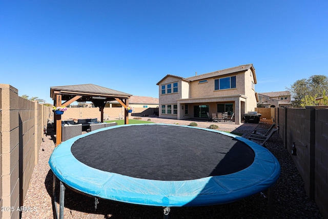 rear view of property featuring an outdoor living space, a trampoline, a gazebo, and a patio area