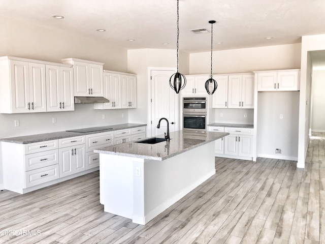 kitchen featuring sink, hanging light fixtures, double oven, a center island with sink, and white cabinetry