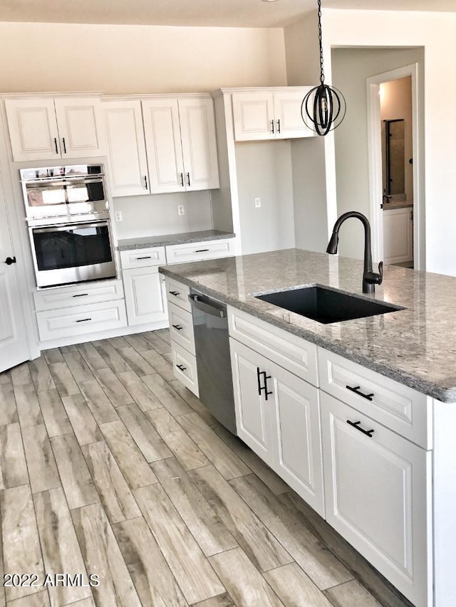 kitchen with appliances with stainless steel finishes, white cabinetry, dark stone countertops, sink, and hanging light fixtures