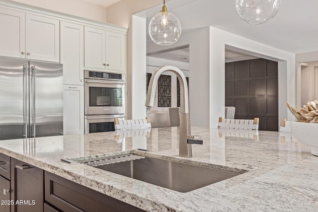 3400 S Whetstone Pl, Chandler, AZ 85286 - kitchen featuring a sink, appliances with stainless steel finishes, light stone countertops, white cabinetry, and decorative light fixtures