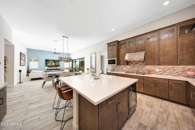 kitchen featuring tasteful backsplash, decorative light fixtures, light wood-type flooring, a kitchen island, and stainless steel gas stovetop