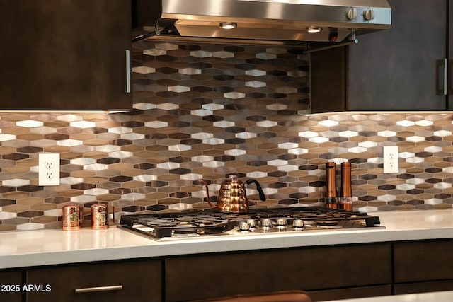 interior space with stainless steel gas stovetop, dark brown cabinets, exhaust hood, and backsplash