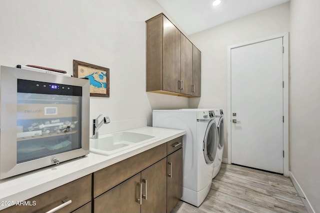 laundry room with cabinets, sink, washing machine and dryer, and light wood-type flooring