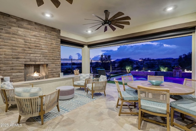 patio terrace at dusk with ceiling fan, a swimming pool, and a brick fireplace