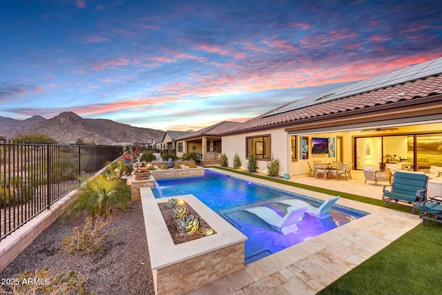 pool at dusk featuring pool water feature, a mountain view, and a patio