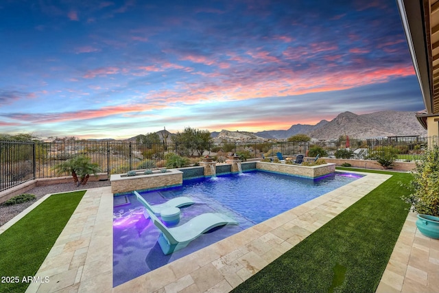 pool at dusk featuring a mountain view, a lawn, pool water feature, and an in ground hot tub