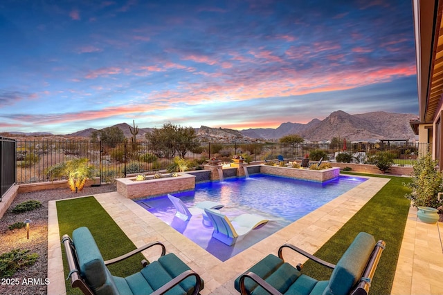 pool at dusk with pool water feature, a yard, a mountain view, and a patio area