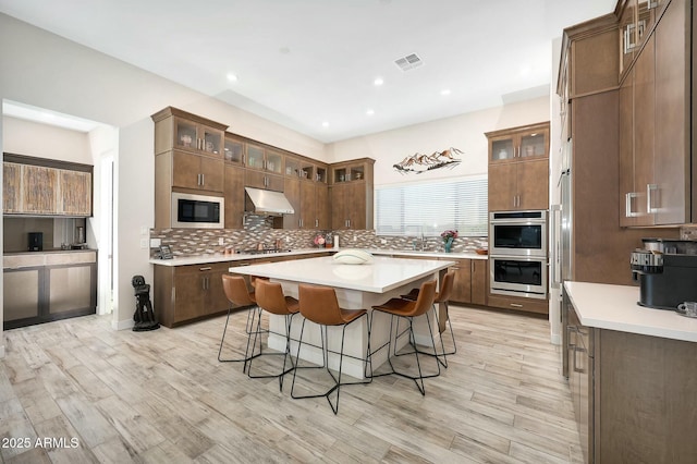 kitchen with double oven, tasteful backsplash, light hardwood / wood-style floors, a kitchen island, and built in microwave